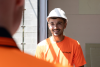 Smiling construction worker in a white hard hat and orange hi-vis shirt on a job site.