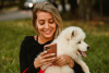 Woman looking at phone while holding dog - Stock.
