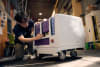 A student engineer inspects a prototype robot designed to keep food hot or cold during delivery
